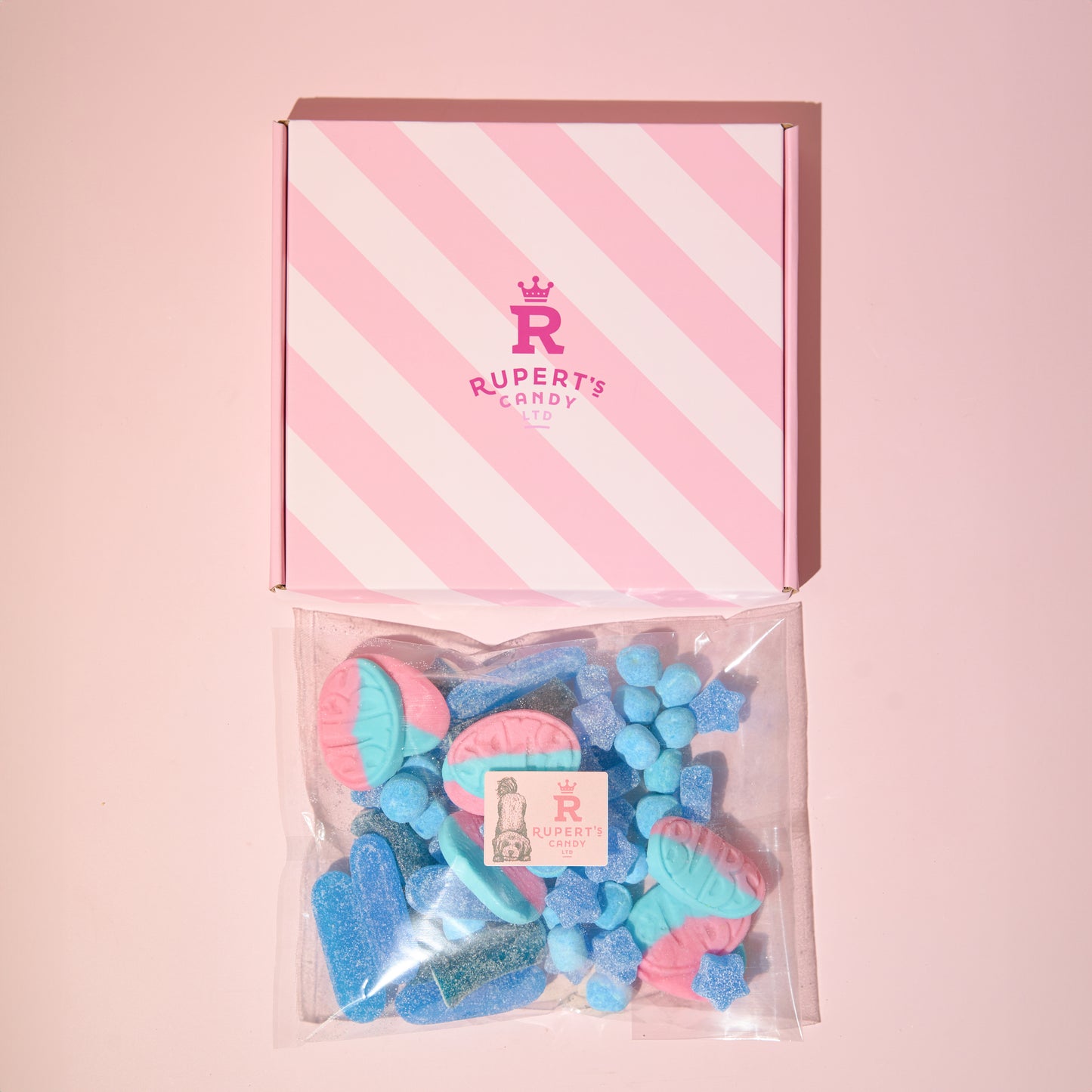 Image of our pink Rupert's candy box with a bag of our blue pick and mix sweets placed laid down underneath it- Rupert's Candy 