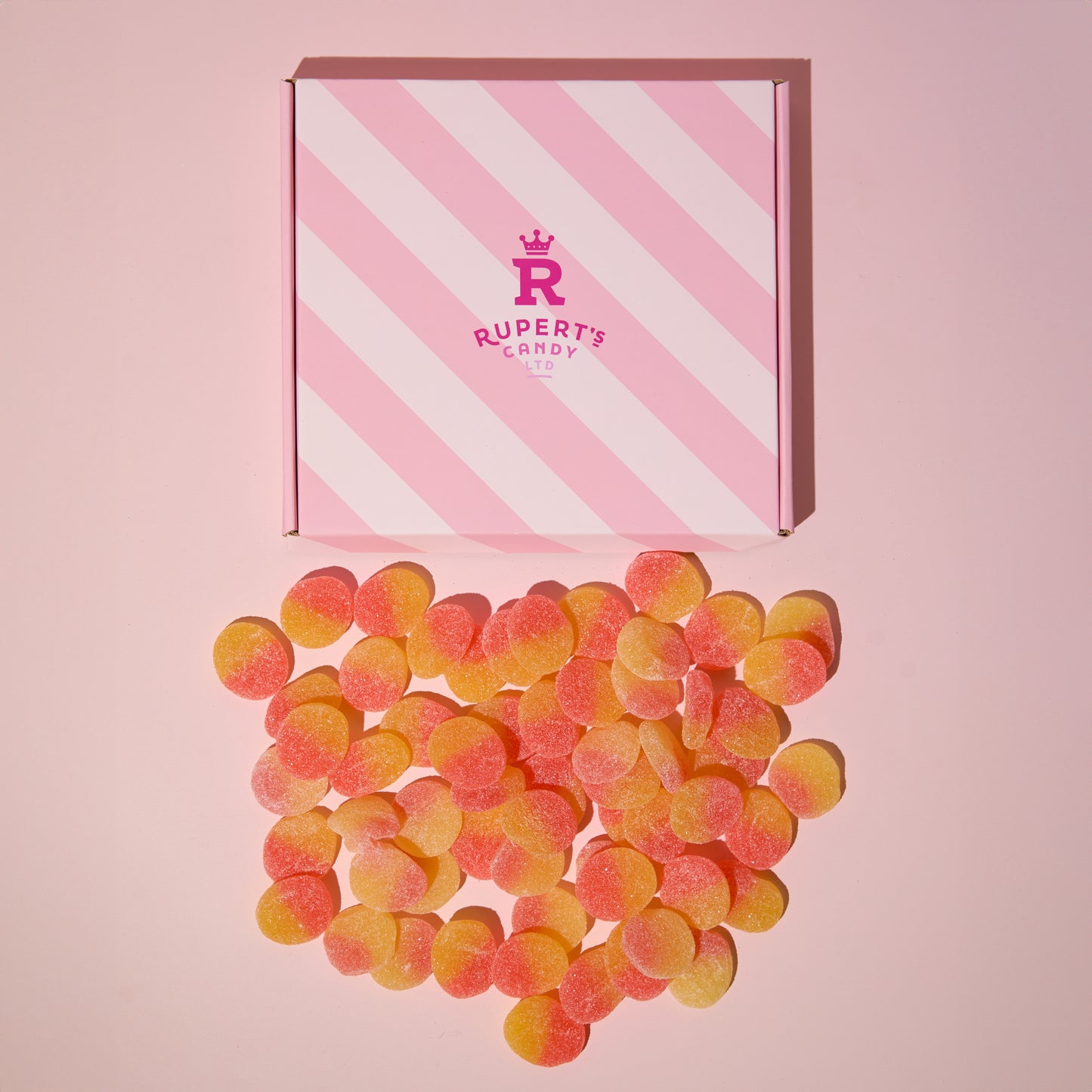 Birds eye view image of our pink Rupert's Candy box with a pile of loose fizzy peaches laid underneath it- Rupert's Candy